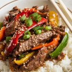 A serving of Crockpot Pepper Steak spooned over a bowl of fluffy white rice