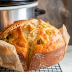 freshly cooked cheddar jalapeño bread being lifted from a slow cooker with parchment paper