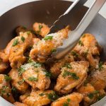 A large bowl filled with crispy garlic Parmesan chicken wings, topped with freshly grated Parmesan and chopped parsley