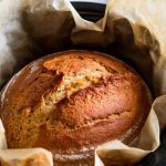 A freshly baked beer bread loaf being lifted out of the slow cooker with parchment paper