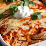 A serving of Crockpot Chicken Enchilada Casserole plated with a dollop of sour cream, fresh cilantro, and extra shredded cheese