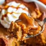 A warm bowl of pumpkin bread pudding, topped with whipped cream and caramel sauce