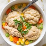 a bowl of homemade crockpot chicken and dumplings, with tender shredded chicken, fluffy dumplings, and colorful mixed vegetables