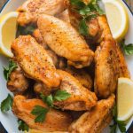 A serving plate of crispy, golden-brown lemon pepper chicken wings garnished with parsley and lemon slices