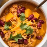 a hearty bowl of Crockpot Pumpkin Turkey Chili, showing tender ground turkey, bright orange pumpkin, red kidney beans, and a sprinkle of shredded cheese