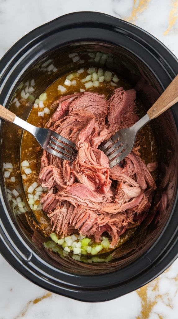 tender pork chunks being shredded with two forks inside the slow cooker