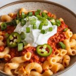 finished chili mac and cheese in a bowl topped with sour cream, chopped green onions, and jalapeños