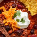 a bowl of slow-cooked brisket chili, showing tender shredded beef, black beans, red kidney beans, and a thick, rich tomato chili base