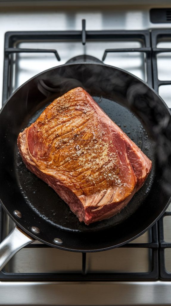 seasoned chuck roast sizzling in a skillet with olive oil, one side golden brown, edges crisping