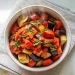 freshly stirred ratatouille being spooned into a bowl, topped with bright green chopped basil