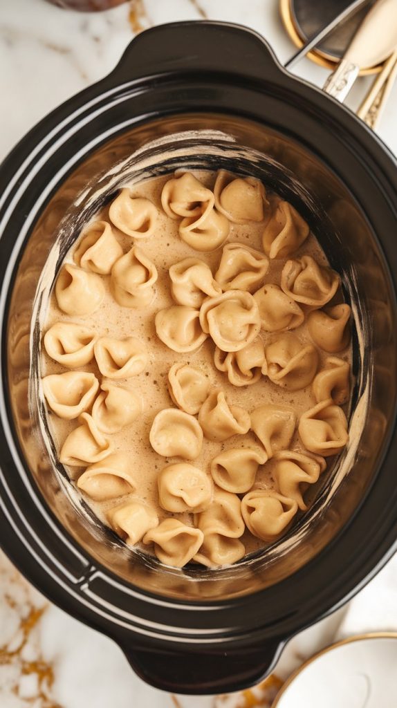 plump cheese tortellini being stirred into the Alfredo cream sauce in the crockpot