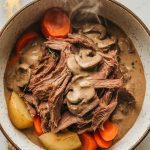 shredded beef, creamy mushroom sauce, carrots, and potatoes served in a white rustic bowl, sauce glistening and thick, steam rising