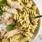 pesto chicken pasta in a white bowl, topped with extra grated parmesan and torn basil leaves