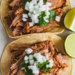 crispy pork carnitas in soft corn tortillas, topped with fresh chopped onion, cilantro, and lime wedge on the side