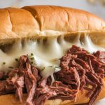 hoagie roll loaded with juicy shredded roast beef, topped with a slice of provolone starting to melt over the hot meat