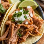 crispy pork carnitas served in soft corn tortillas, topped with freshly chopped cilantro, diced onions, and lime wedges on the side
