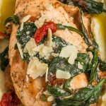 creamy Tuscan chicken served over mashed potatoes, with sauce running down the sides, sun-dried tomatoes and spinach visible, and extra Parmesan sprinkled on top