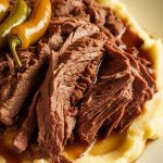 shredded Mississippi Pot Roast served on a bed of creamy mashed potatoes, topped with a drizzle of cooking juices and a few whole pepperoncini peppers