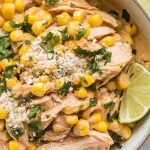 Crockpot Mexican Street Corn Chicken served in a shallow bowl, garnished with crumbled cotija cheese, lime wedges, and fresh cilantro