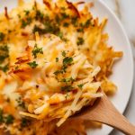 cooked cheesy hashbrowns being stirred with a wooden spoon, melted cheese stretching slightly, then garnished with chopped parsley