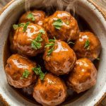 a bowl filled with glazed bourbon apple butter meatballs, each meatball glossy and coated in thick, sticky sauce