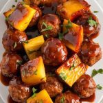 a white plate filled with glossy BBQ meatballs and pineapple chunks
