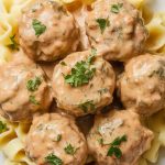 creamy Swedish meatballs served on buttered egg noodles, parsley sprinkled on top, sauce glistening and thick, meatballs perfectly coated