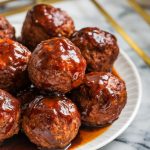 several raspberry balsamic glazed meatballs casually arranged on a clean white ceramic plate