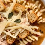 finished Chicken Parmesan Soup in a white bowl, topped with golden croutons, melted cheese strands, and fresh basil