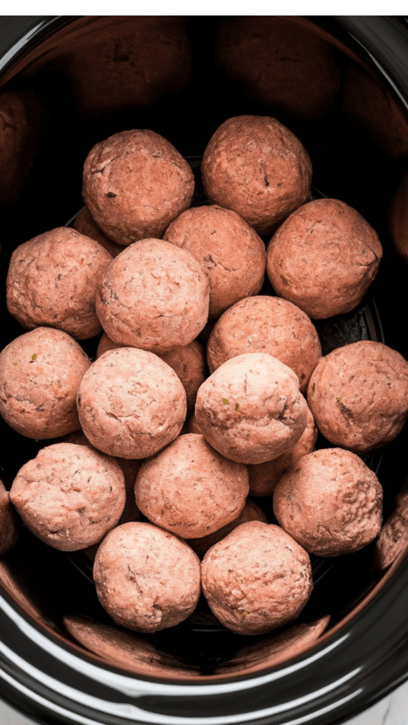 frozen fully-cooked meatballs piled into a black ceramic slow cooker