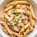 plated garlic parmesan chicken pasta in a white bowl, garnished with parsley and extra cheese, creamy sauce glistening