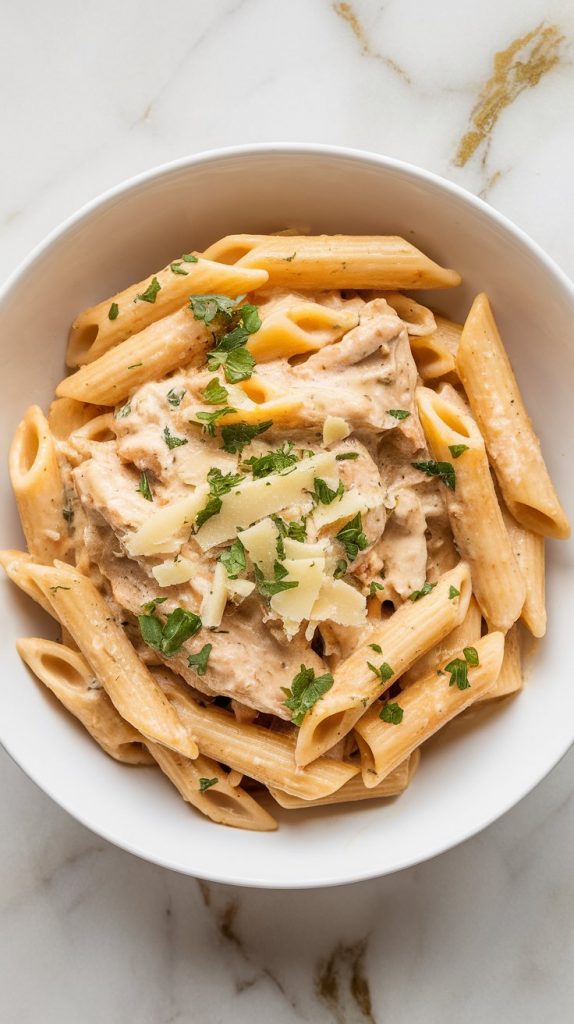 plated garlic parmesan chicken pasta in a white bowl, garnished with parsley and extra cheese, creamy sauce glistening