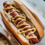 a hot dog in a bun, piled with tender sauerkraut and onions, mustard drizzled on top, and steam rising