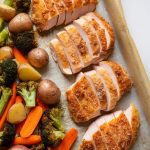 a parchment-lined sheet pan just out of the oven, with four golden, crispy Parmesan-crusted chicken breast halves arranged tightly in a neat row on one side