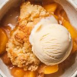 a warm scoop of peach cobbler served in a shallow white ceramic bowl